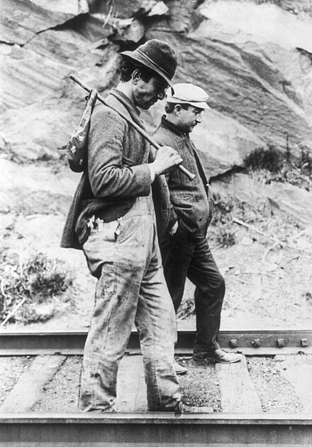 Two hobos walking along railroad tracks, after being put off a train. One is carrying a bindle.