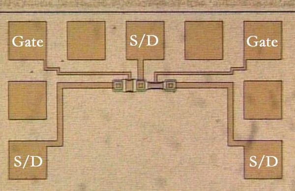 Photomicrograph of two metal-gate MOSFETs in a test pattern. Probe pads for two gates and three source/drain nodes are labeled.