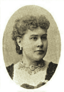 B&W portrait photo of a woman with short wavy hair, wearing earings, decorative choker necklace, and dark top