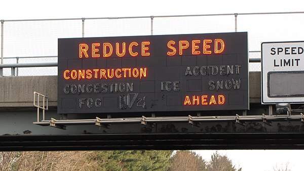 Early style of VMS on the New Jersey Turnpike using neon tubes, since replaced by new LED VMS signs. It is next to a vane variable speed-limit sign