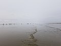 Playa de marea baja bajo un cielo nublado con diminutas siluetas de personas en la distancia