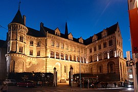 Fotografia de um imponente edifício medieval, em tufo, iluminada à noite.  Uma torre à sua esquerda