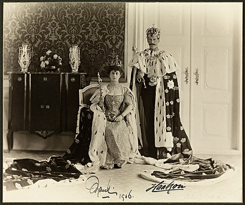 Offisielt kroningsbilde av kong Haakon VII og dronning Maud iført kronregalier og britiske kroningskapper i hermelin og fløyel. Fotografiet er tatt i Dronningens sal i Stiftsgården etter kroningen i Nidarosdomen 22. juni 1906. Det er den siste kroningen som har funnet sted i Norge.