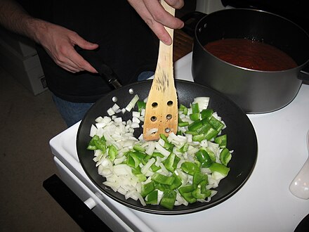 A cook sautees onions and green peppers in a skillet.