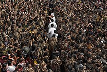 A group of devotees covered in mud gathering as a line of men in white robes travel through.