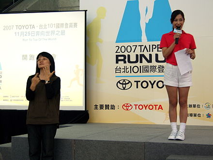 The hostess (in red) and a sign language interpreter at a press conference in Taipei, 2007.