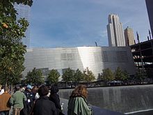 Silberfarbenes Gebäude mit quadratischem Wasserfall im Vordergrund und Wolkenkratzern im Hintergrund