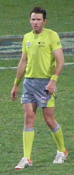 A man in a yellow shirt and shorts stands on grass