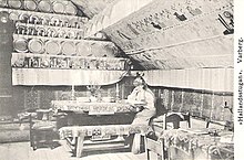 Interior of Bexell Cottage, early 20th century. Pictured is Herdis Bexell, a relative of Alfred Bexell Bexellska stugan vykort.jpg