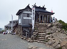 Eine Steintreppe führt zu einer Hütte, welche auf einem Berg steht.