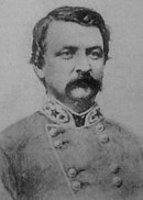 Black and white photo shows a man with a moustache wearing a gray military uniform with two rows of buttons. The insignia on the collar indicates a Confederate general officer.
