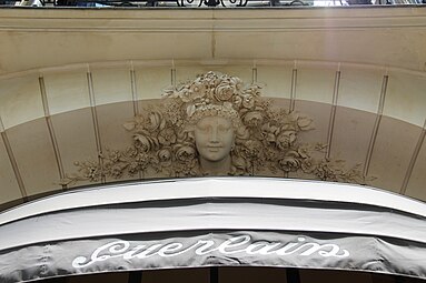 Beaux Arts mascaron with a multitude of flowers around it, above a window of the parfumery of Jacques and Pierre Guerlain, (Avenue des Champs-Élysées no. 68), Paris, designed by architect Charles-Frédéric Méwès and decorated by Bérard Christian, 1912[48]