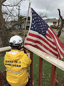 A member of Texas Task Force 1 re-hoists a fallen US flag in Rockport, Texas, following landfall of Hurricane Harvey in 2017. RockPort HARVEY 8-27-2017.jpg