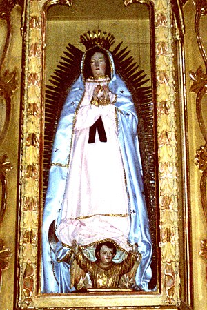 La Virgen de Guadalupe, in the Church of Santa María Asunción Tlaxiaco, Oaxaca, Mexico, in a glass case in the center of the retablo of the first altar along the left wall of the nave.