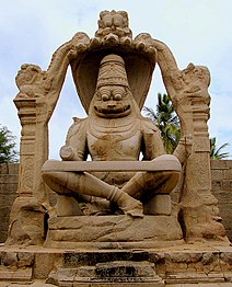 Brown stone statue of smiling deity sitting cross-legged under arch