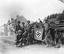 Lined up in front of a wrecked German tank and displaying a captured swastika, is a group of American infantrymen who were left behind to "mop-up" in Chambois, France, last stronghold of the Nazis in the Falaise Gap area, August 20, 1944. Yank infantrymen in Chambois.jpg