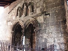 Photo d'un tombeau sculpté. Il comporte deux arches en arc brisé trifolié et une statue décapitée. Le fronton au-dessus, est composé de trois niches séparées de deux petites colonnes abritant des statues.