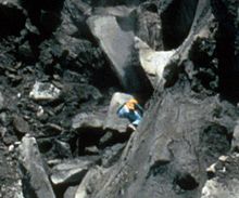 Un homme escaladant une falaise abrupte éclipsé par d'énormes rochers autour de lui.