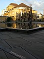 Gedenkbrunnen auf dem Platz der Alten Synagoge in Freiburg mit neu angebrachtem Bronzeband, das zum Erinnern an die zerstörte Synagoge an diesem Platz anhalten soll, im Hintergrund das Stadttheater