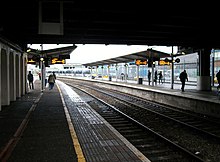 Foto entlang zweier gebogener Bahnsteige, aufgenommen unter einem Schutzdach und mit Blick ins Tageslicht.
