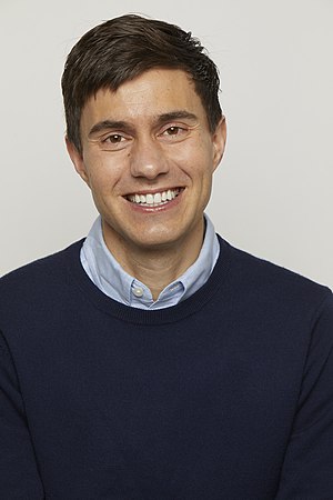 Headshot-style image of Ricky Van Veen wearing a sweater over a blue button-up shirt
