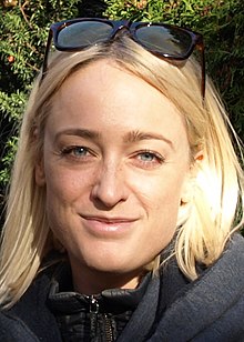 white female with dyed blond hair, smiling at camera, with sunglasses perched on top of head
