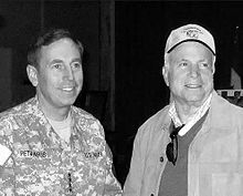 Middle-aged man in military uniform talking with older man in casual civilian clothes, at night