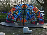 Outdoor sculpture; a public glass object in bright colors at the city square Frederiksplein, Amsterdam; free photo of Fons Heijnsbroek, January 2022