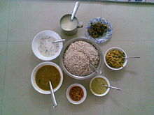 Sadya items ready to be served, clockwise from top: paayasam, bittergourd thoran, aviyal, kaalan, lime pickle, sambar; buttermilk with boiled rice in the center Sadhya Items.jpg