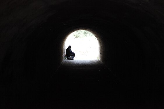 An elderly woman sits at the end of a tunnel