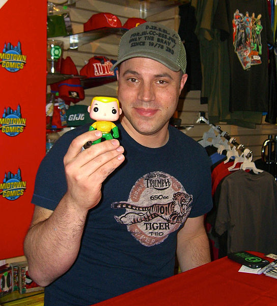 Johns holding up a Funko vinyl figure of Aquaman, one of the titles he wrote as part of The New 52