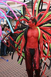 uomo a torso nudo, la pelle dipinta di rosso, con palloncini sulla schiena che sembrano tentacoli