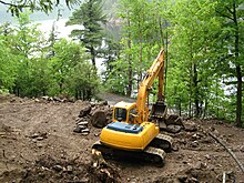 Excavator clears woodland on the shoreline of a lake