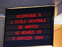 Tableau électronique dans une école qui affiche « Bienvenue à l’école centrale de Nantes, 12 heures 09, 3 janvier 1900 ».