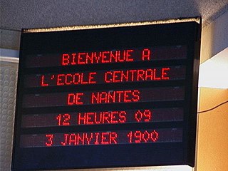 Tableau électronique dans une école qui affiche « Bienvenue à l’école centrale de Nantes, 12 heures 09, 3 janvier 1900 ».