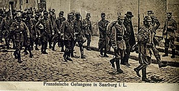 Photo d'une colonne de prisonniers, officiers en tête et encadrés par des gardes.
