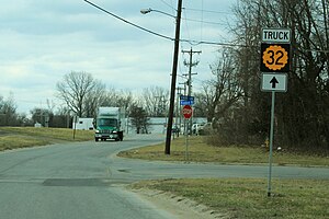 A two-lane road in a developed but semi-rural area. A sign advises trucks to continue straight for K-32 Truck.