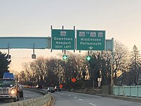 Road signs and traffic on a highway at dusk, with directions to Downtown Newport and Middletown/Portsmouth