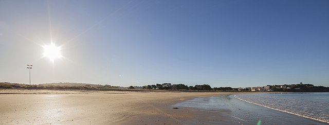 Playa Grande de Miño con sol, donde a la derecha se ve el mar, que está en marea baja, y a la izquierda el sol y la playa.