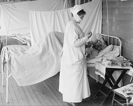 A nurse wears a cloth face mask while treating a flu patient in Washington, DC, c. 1919