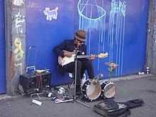 Musician in London performs on electric guitar and a small drum kit Guitarist Liverpool Street.JPG