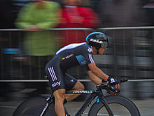 Photographie d'un cycliste, vu de profil, en noir et bleu foncé.