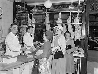 Photo en noir et blanc de l'intérieur d'une boucherie, où on compte deux hommes bouchers et plusieurs femmes clientes.