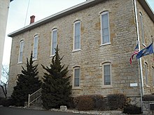 Von der Straße aus ist ein Steingebäude zu sehen, daneben ein Fahnenmast;Dies war eines der Gebäude der Lane University in Lecompton, Kansas.