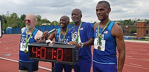 Four older sportspeople on a track, bearing medals