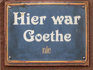 Plakette oder Tafel an einer Wand mit der Aufschrift: „Hier war Goethe nie“. Das letzte Wort „nie“ ist kleiner und unauffälliger gestaltet, als die ersten drei Wörter.