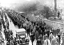 Fekete-fehér fénykép egy oszlop zsidó férfiakról, akiket a pogrom után tartóztattak fel Baden-Badenben