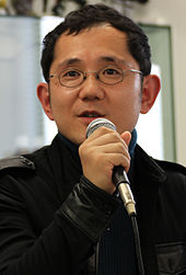 A 2011 photograph of Shu Takumi, holding a microphone