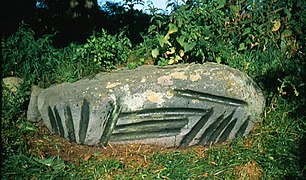 Una piedra con surcos que ha sido puesta en el borde de una tumba prehistórica. Los surcos están en el lado de la piedra (Gotland)