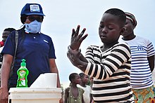 Building a culture of handwashing with children can create a change in culture with widespread public health benefits. Supervising a young boy washing his hands.jpg